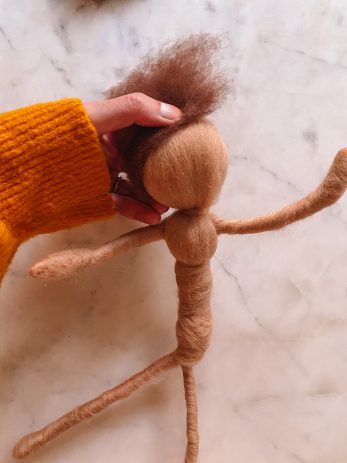 A person holding the top of a handmade doll